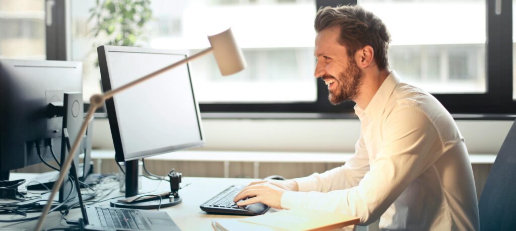 Mann sitzt an Schreibtisch vor einem Computer.